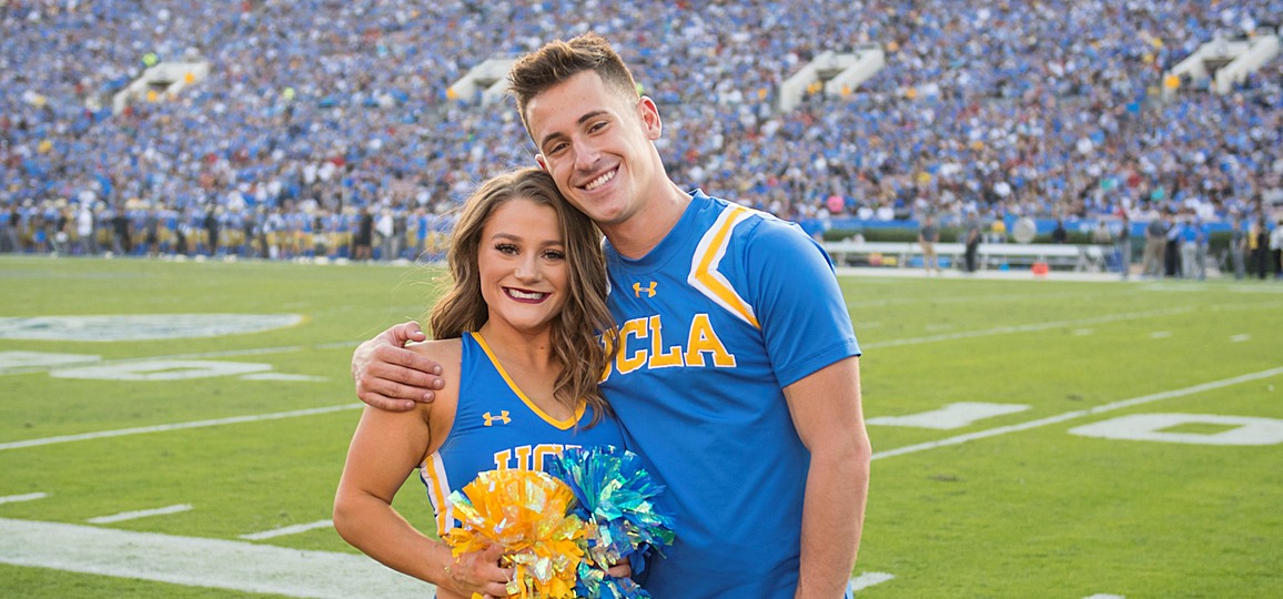 One male and one female member of the UCLA Cheer Team wearing blue uniforms and standing together on the field at the Rose Bowl
