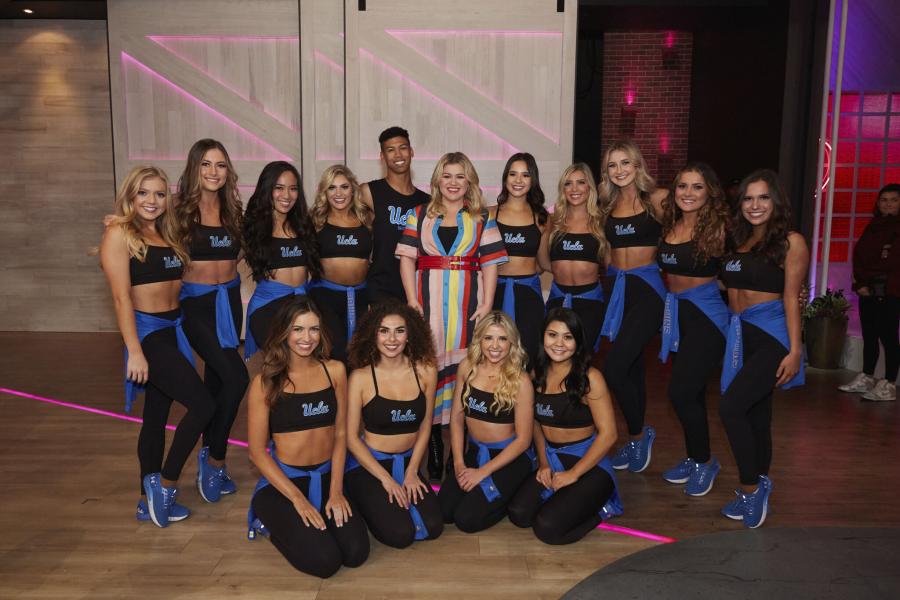 Members of the UCLA Dance Team posed with Kelly Clarkson after performing on her daytime talk show.  Dance Team members are wearing black sports bras and black leggings.