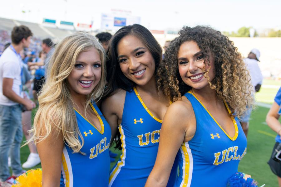 Three women from the UCLA Dance Team posing in their blue uniforms while performing on the field at the Rose Bowl during the UCLA / Oklahoma football game.