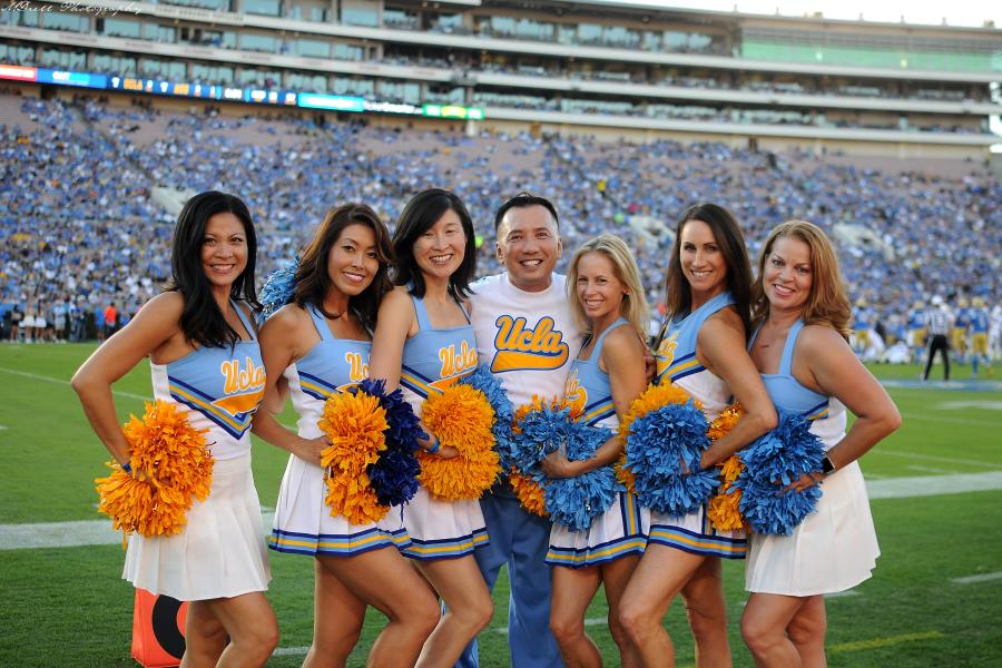 Seven alumni of the Spirit Squad in their original blue and gold uniforms, posing on the field at the Rose Bowl during the Homecoming game.